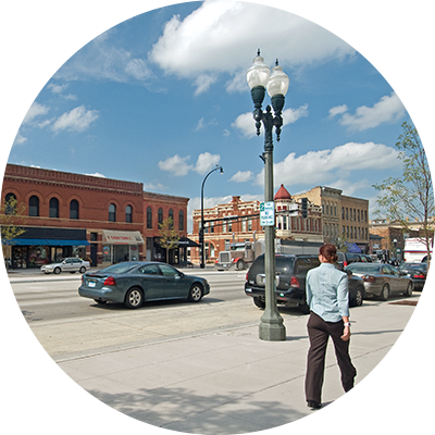 Image of a pedestrian walking along a street with parked cars in St. Peter, MN.